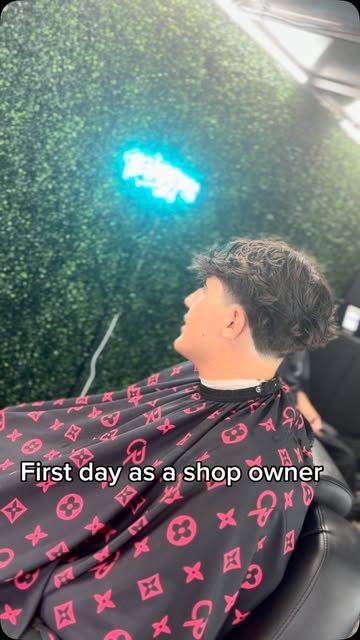 Jake's first client at Cashed Out Lounge in a red LV-pattern cape, with a neon sign on a green hedge wall behind him