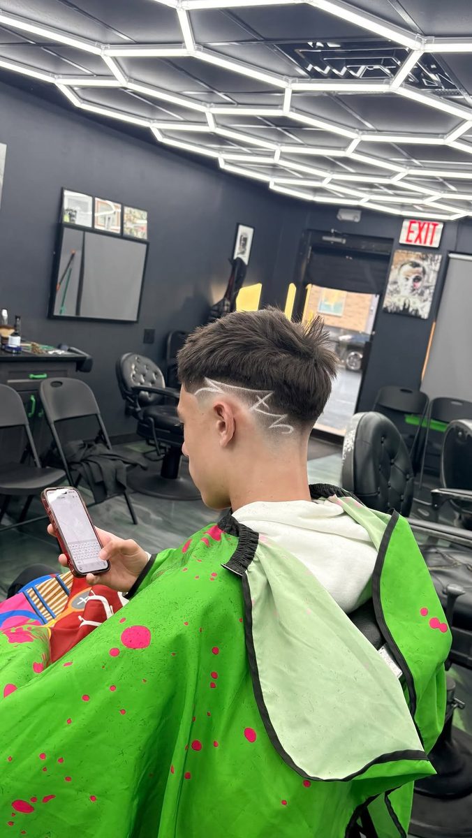 Client on his phone in the chair with a sharp line design cut into a fade