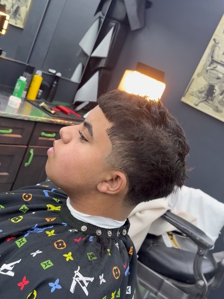 Side profile of a taper with a textured top, client in a black cape with a colorful monogram print